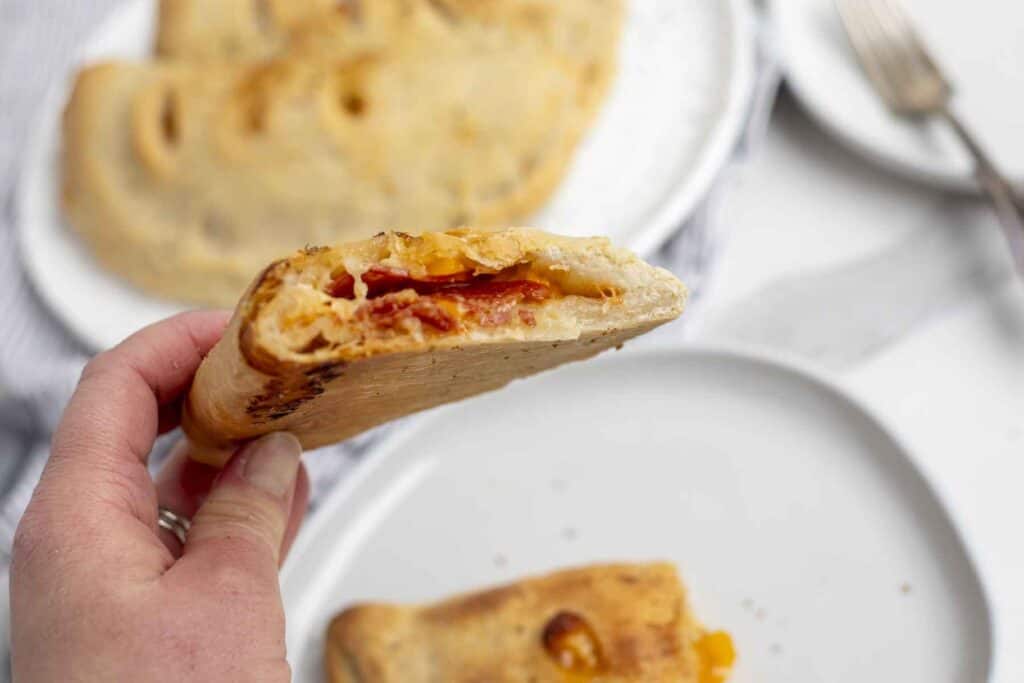 hand holding a half of a calzone up with more calzones on plates in the background