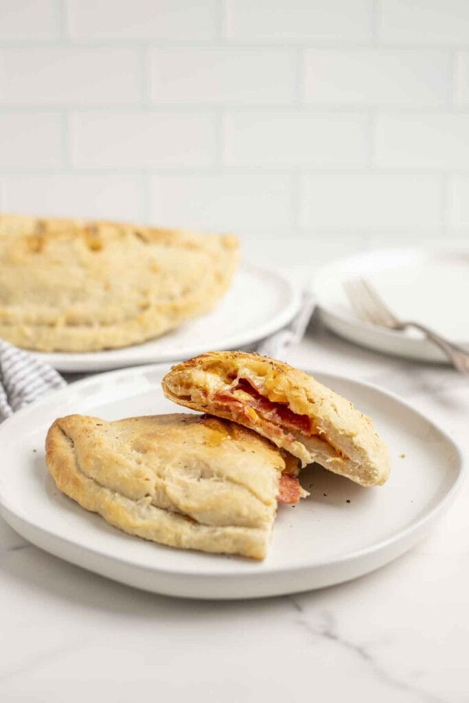 a calzone made with sourdough pizza dough sliced in half on a cream colored plate with more calzones in the background