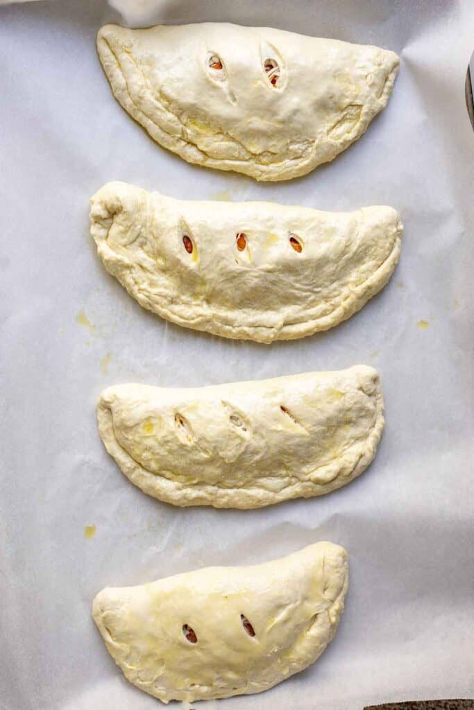 four unbaked calzones on a baking sheet lined with parchment paper