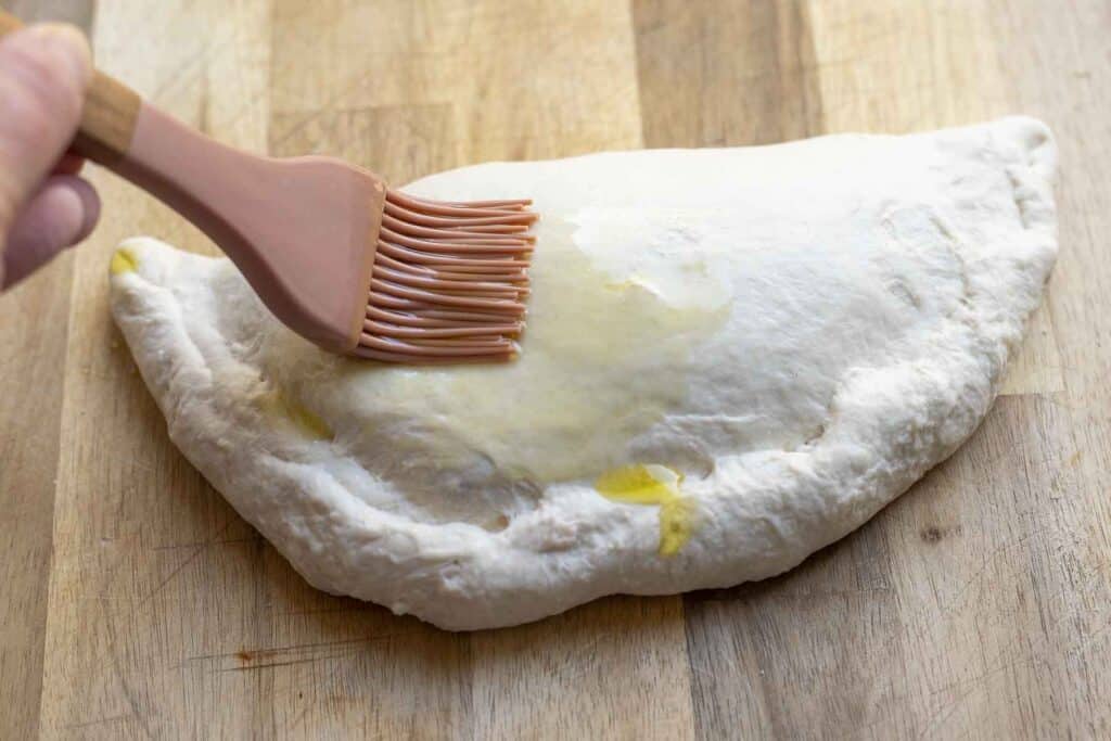 spreading olive oil onto a calzone with a silicon brush on a wood cutting board