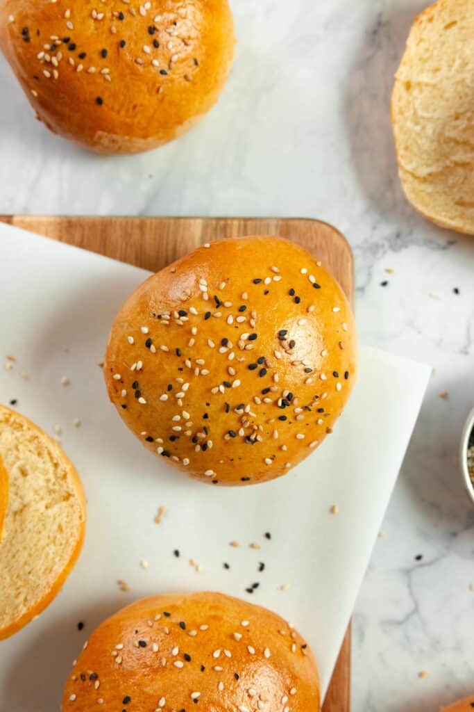 overhead photo of sourdough hamburger buns made with discard on a marble countertop, a cutting board with a plate on top