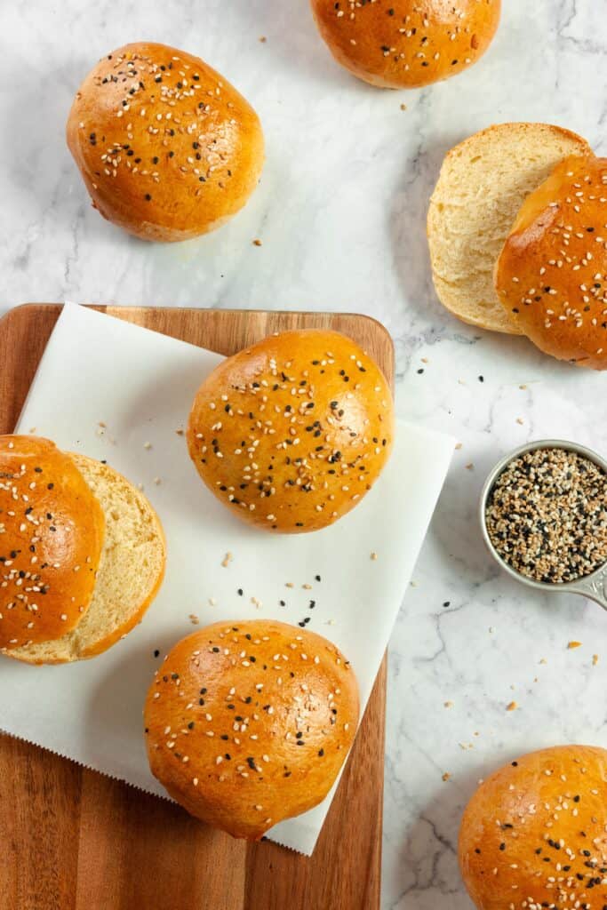 six sourdough discard hamburger buns scattered on a marble countertop and wood cutting board