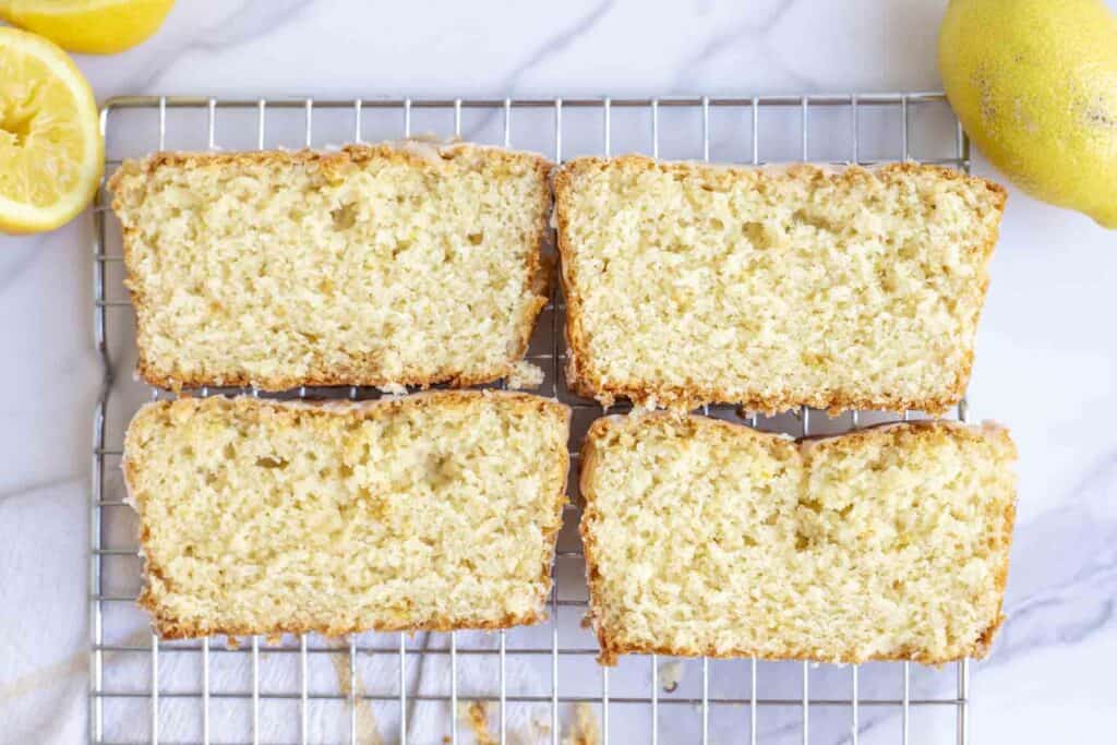 four pieces of lemon sourdough bread on a wire rack on a marble counter surrounded by lemons