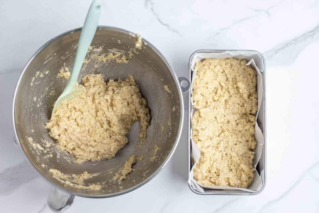 batter being added to a loaf pan lined with parchment paper.