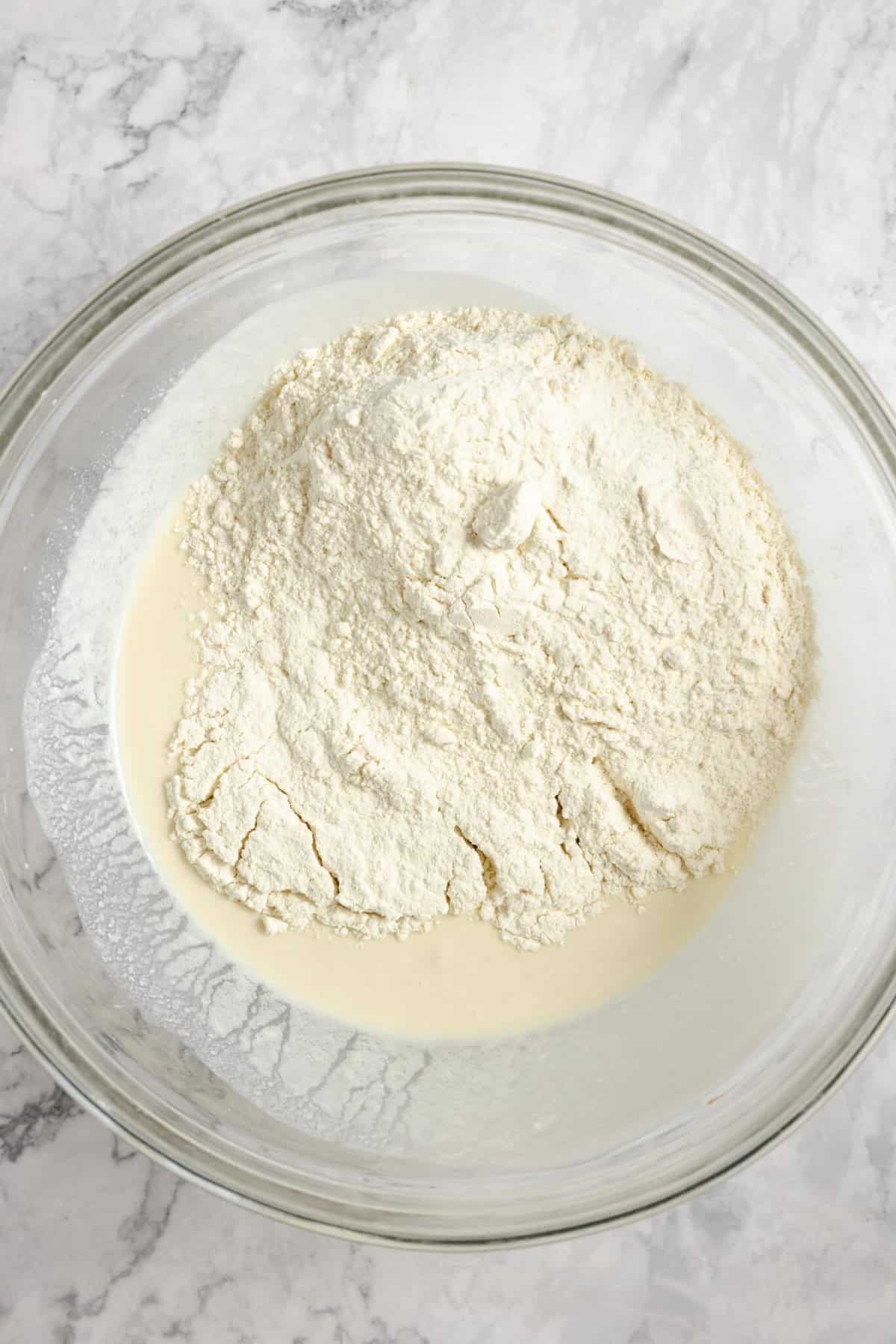 the dry ingredients for sourdough naan in a large glass bowl on a white countertop