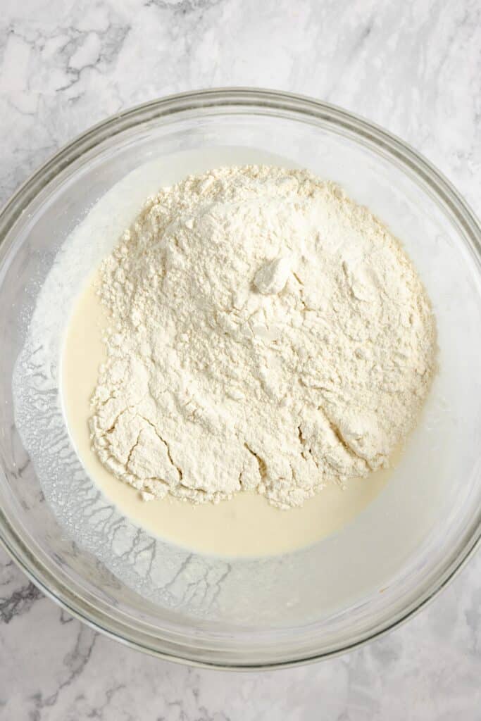 the dry ingredients   for sourdough naan in a large glass bowl on a white countertop