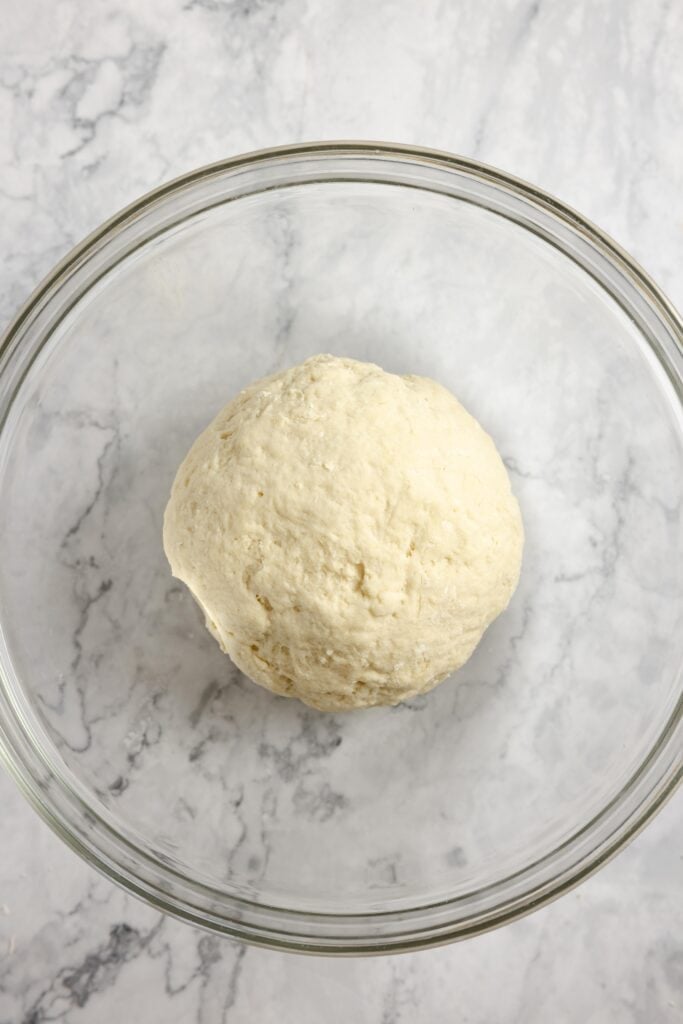 sourdough naan dough ball in a large glass bowl ready to rest