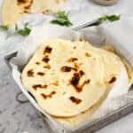 sourdough naan stacked in a square baking dish lined with parchment paper