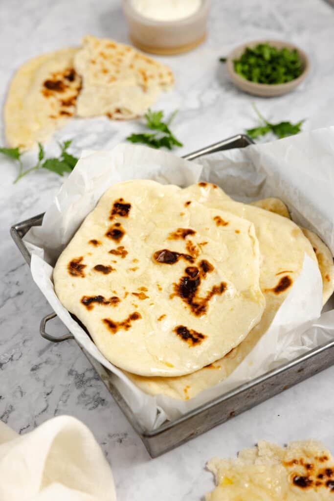 sourdough naan stacked in a square baking dish lined with parchment paper