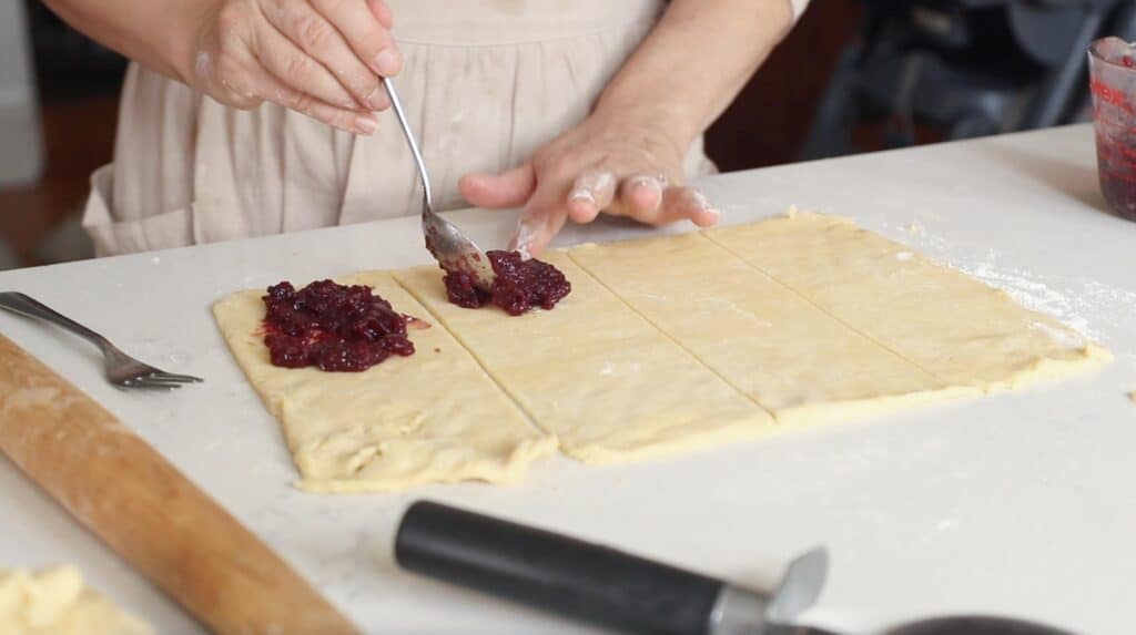 two hands adding jam to a sourdough poptart dough with a silver spoon