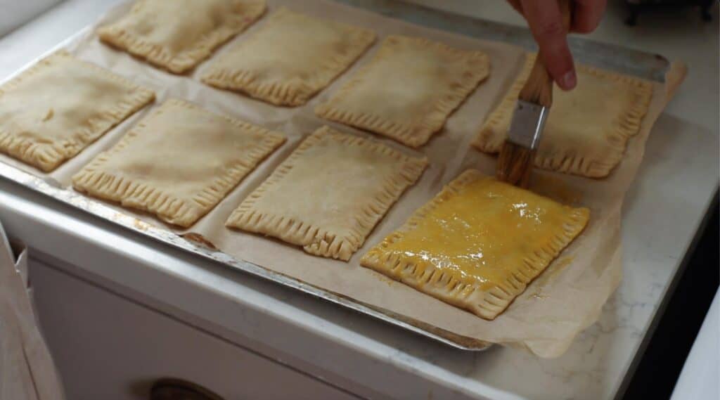 someone brushing an egg wash on a sourdough poptart with a pastry brush