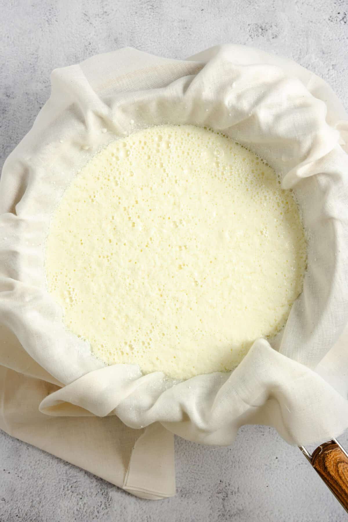 straining ricotta cheese through cheese cloth and a strainer.