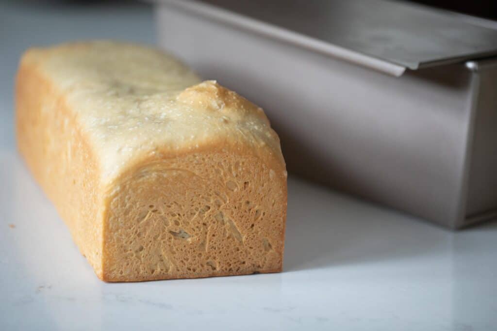 A loaf of pain de mie next to a pullman pan on a white countertop