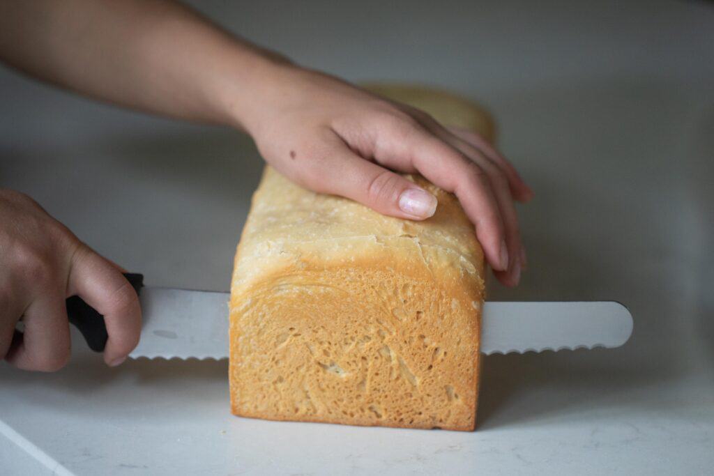 two hands slicing a loaf of pain de mie bread on a white countertop