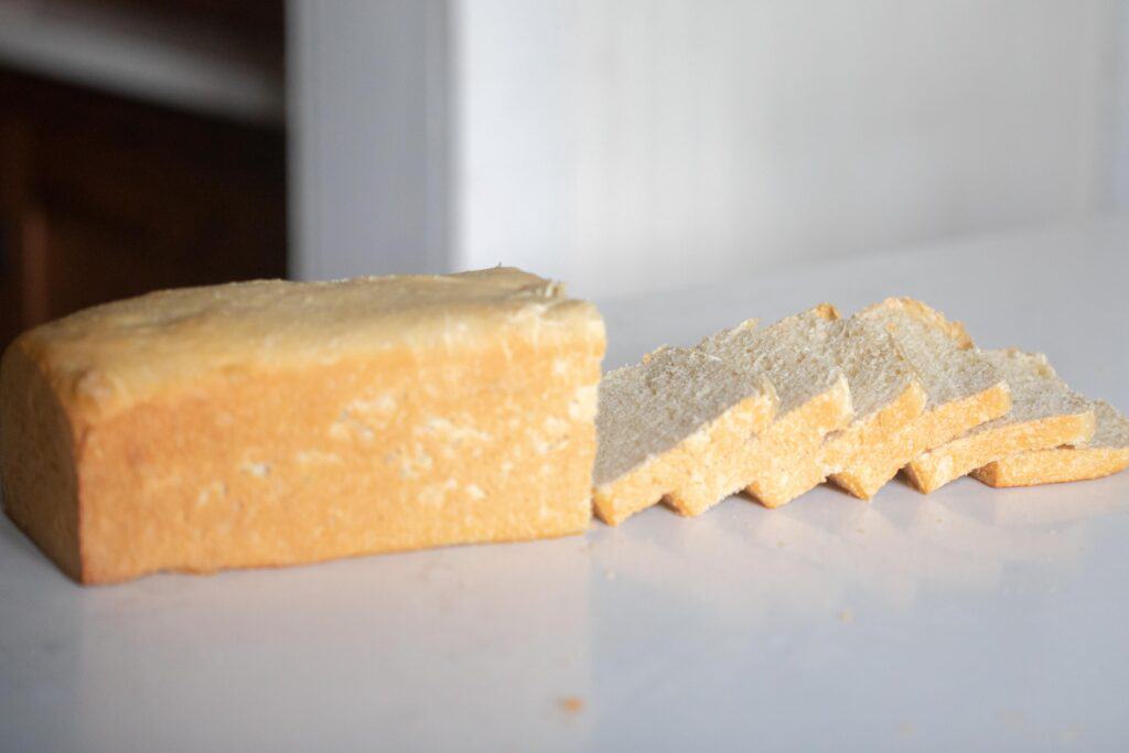 A loaf of pain de mie bread on a white countertop with half of it cut into slices layered on top of one another