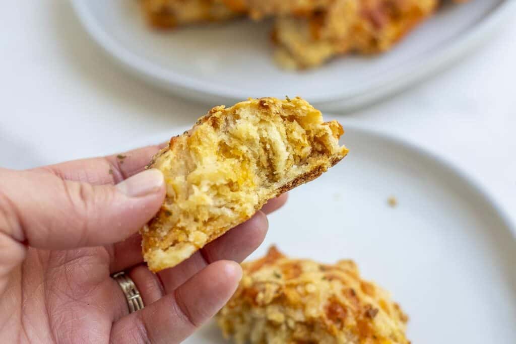 a hand holding half of a sourdough cheddar biscuit to show the fluffy interior with a white plate in the background