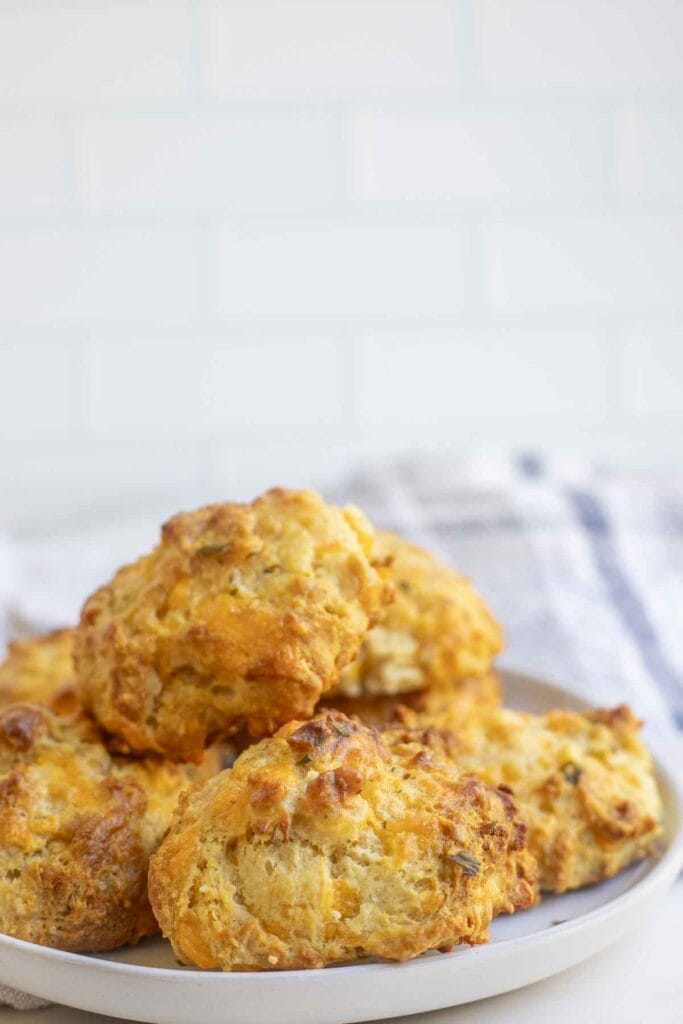 A plate full of sourdough cheddar biscuits with a tea towel in the background