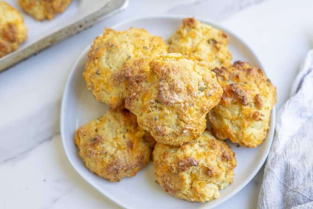 A white plate full of sourdough cheddar biscuits on a white countertop