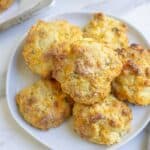 A white plate full of sourdough cheddar biscuits on a white countertop