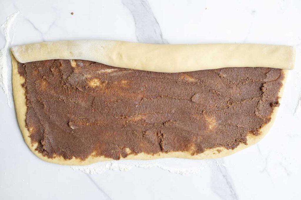 rolling up dough with cinnamon, sugar, and butter spread on the dough