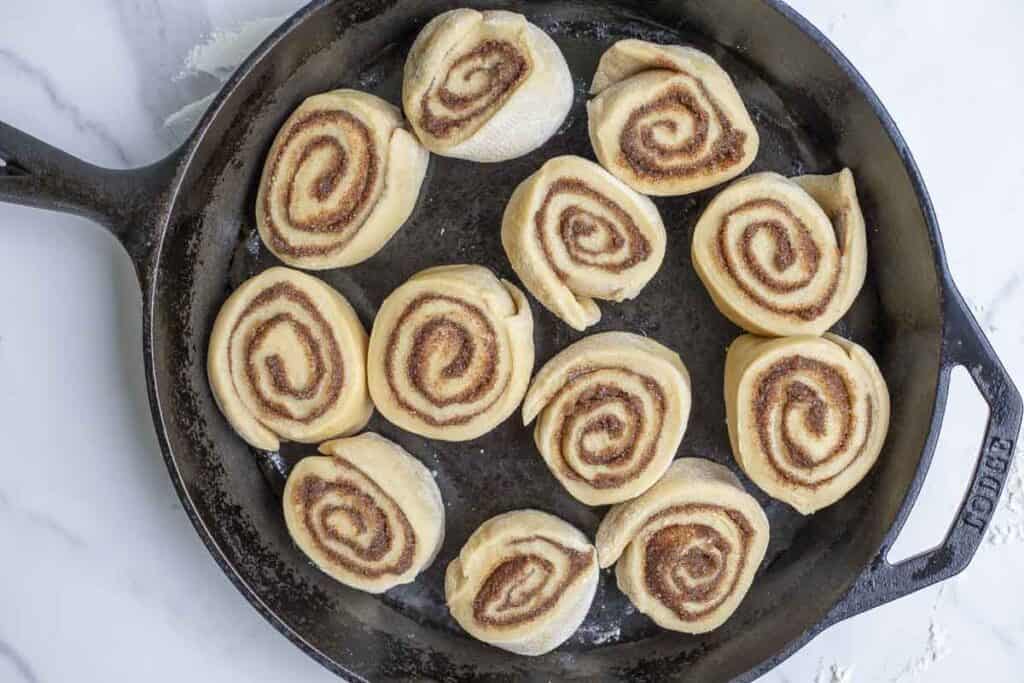 unbaked sourdough discard cinnamon rolls in a cast iron skillet on a marble countertop