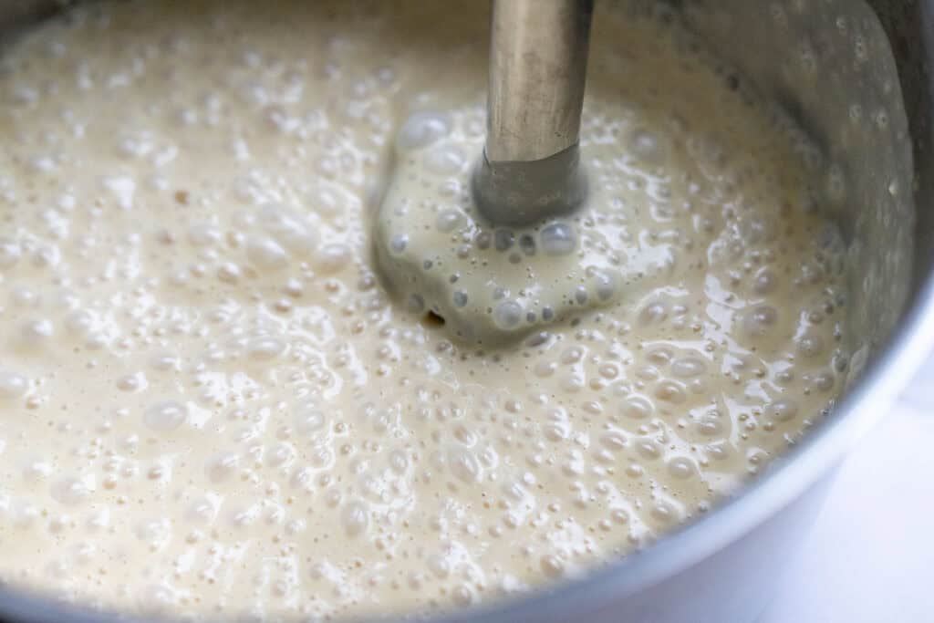 blending up cream cheese frosting in a saucepan with a immersion blender