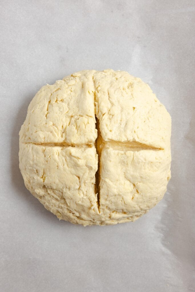 sourdough Irish soda bread dough with a x scored on top. The dough is on parchment paper