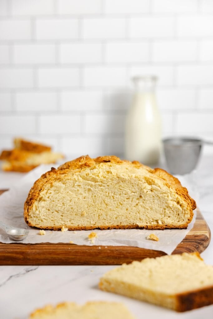 a side view of a half of loaf of sourdough Irish soda bread on a parchment lined cutting board.