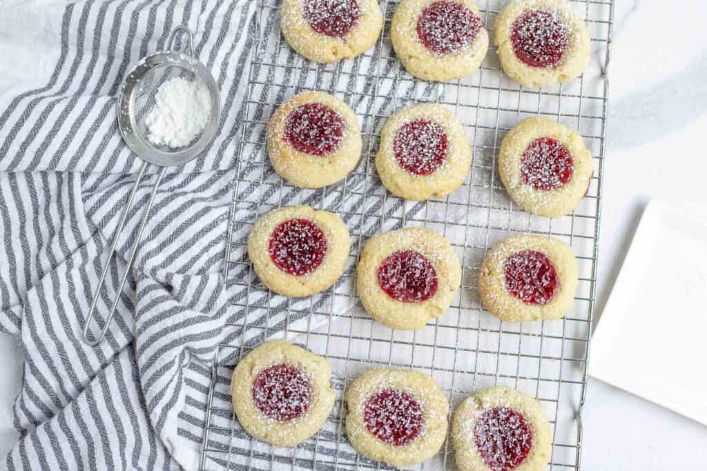 12 sourdough thumbprint cookies on a wire rack over a white and black striped towel