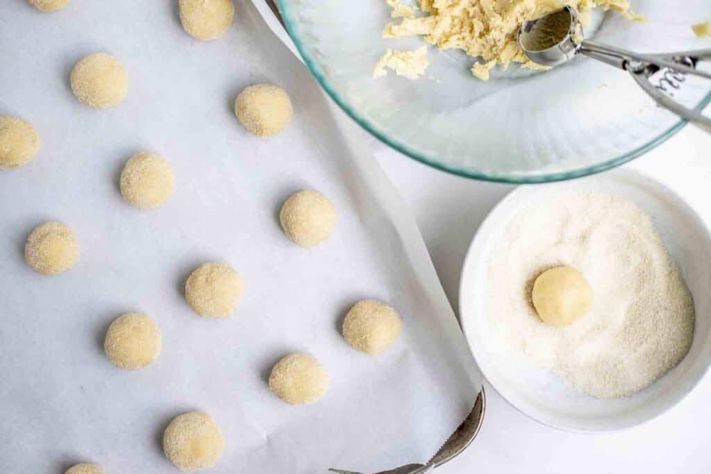 sugar cookie dough balls on parchment paper. Sugar is in a bowl to the right