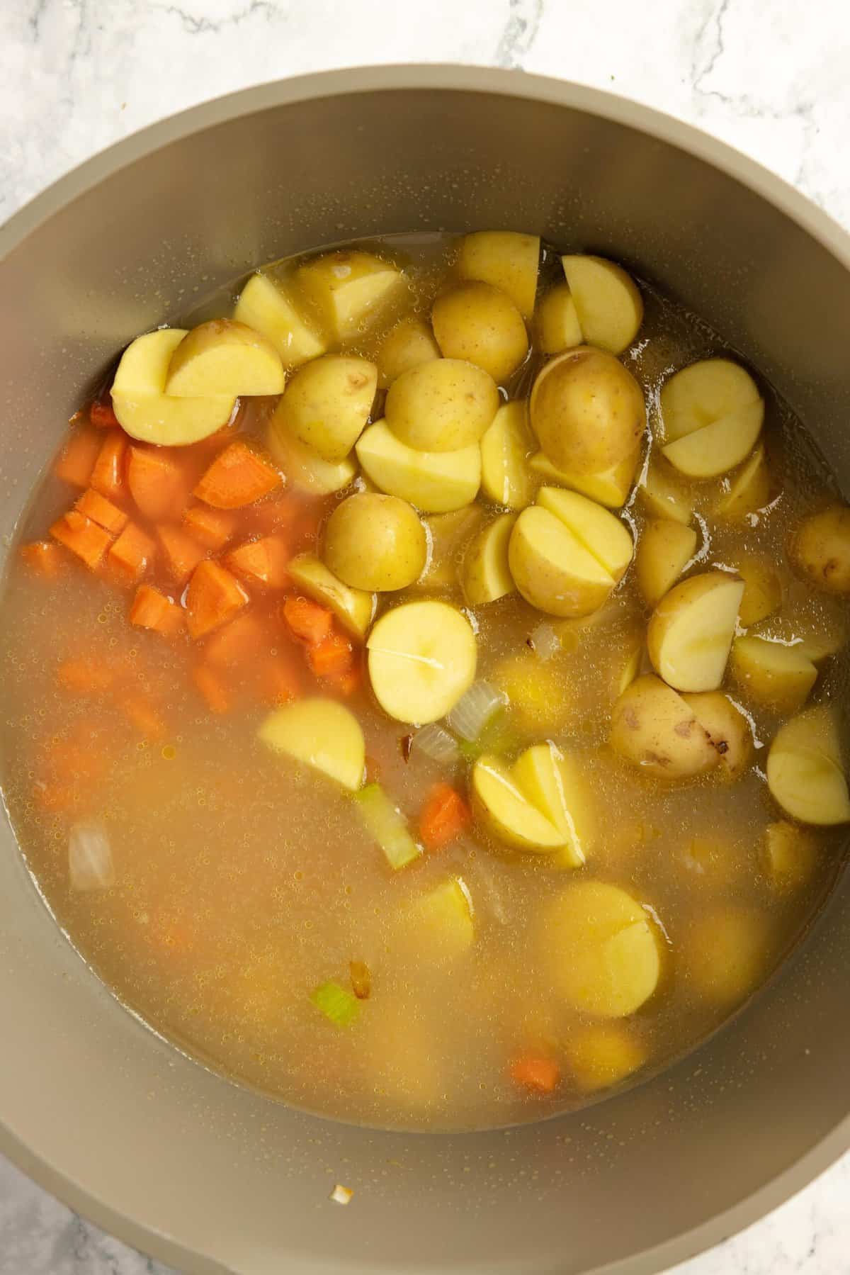 Broth carrots and potatoes added to a Dutch oven. 