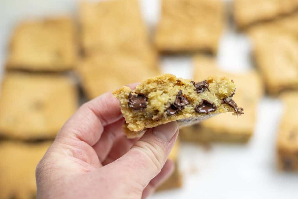 hand holding a sourdough blondie with a bite taken out. More blondies are in the background