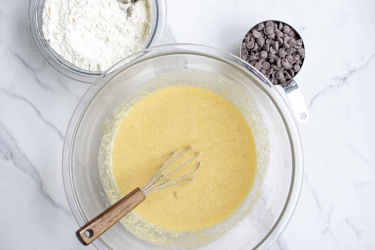 wet ingredients in a glass bowl with dry ingredients and chocolate chips in separate bowls.