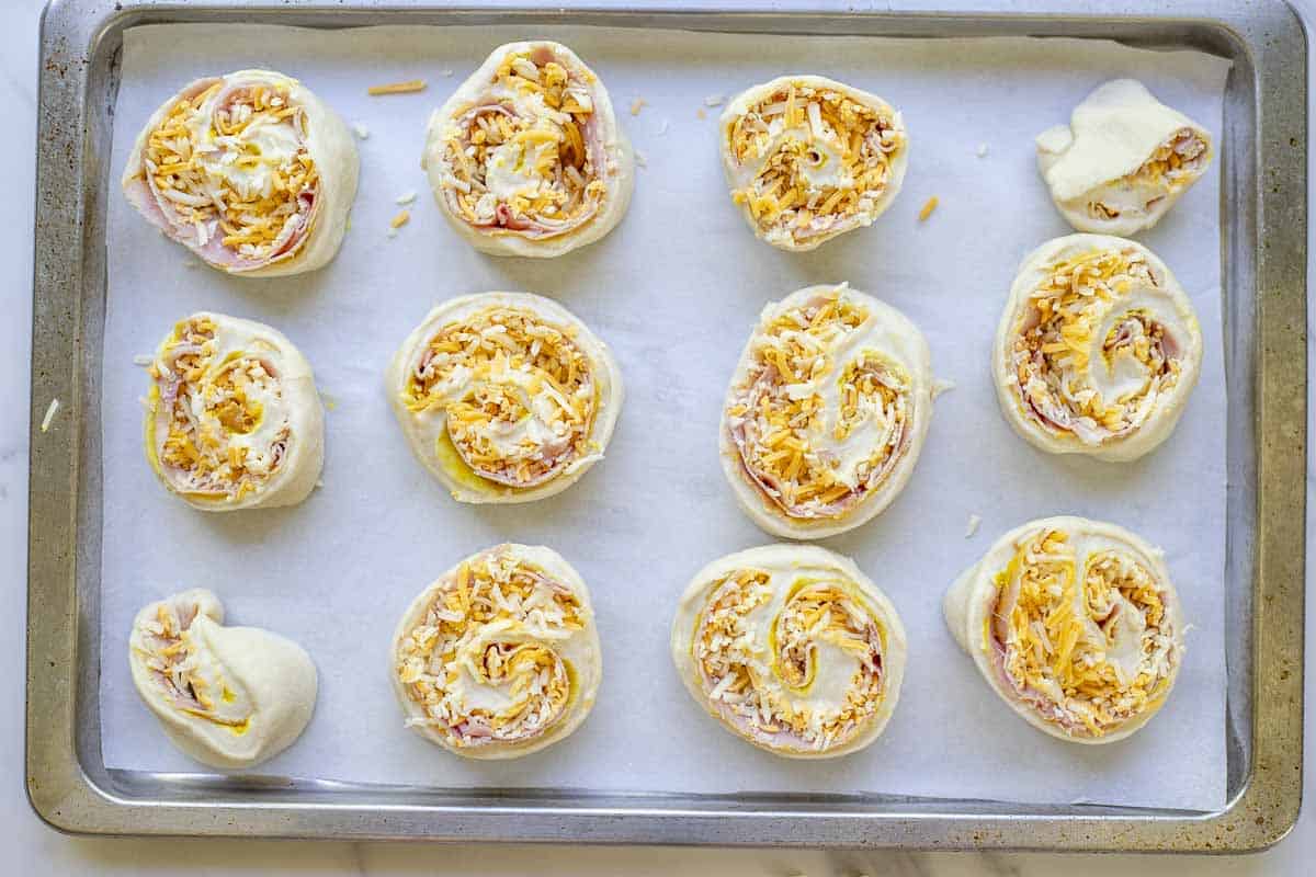 Unbaked sourdough ham and cheese rolls on a parchment paper lined baking sheet