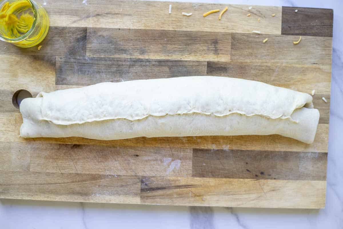 sourdough ham and cheese rolls rolled up and ready to be cut into pinwheels on a wooden cutting board.