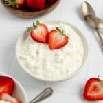 cottage cheese in a bowl with strawberries, more strawberries surround the bowl.