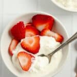 spoonful of cottage cheese coming out of a bowl with strawberries.