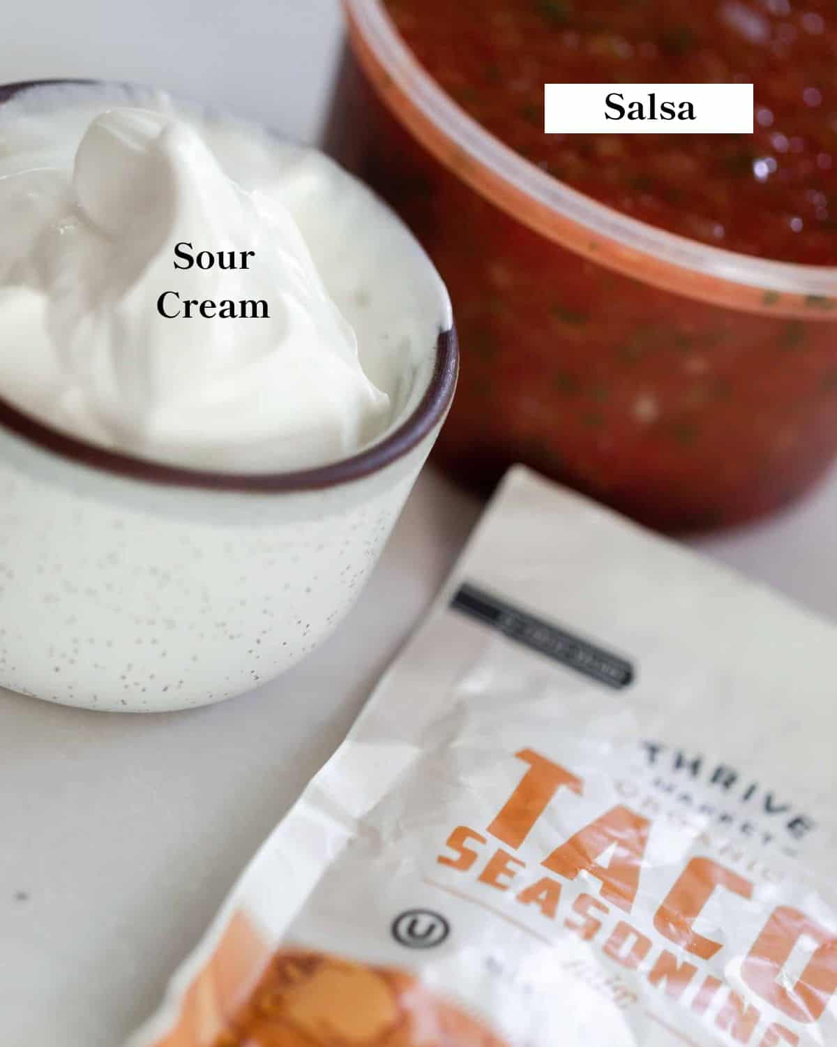 A container of sour cream, salsa, and a packet of taco seasoning. 