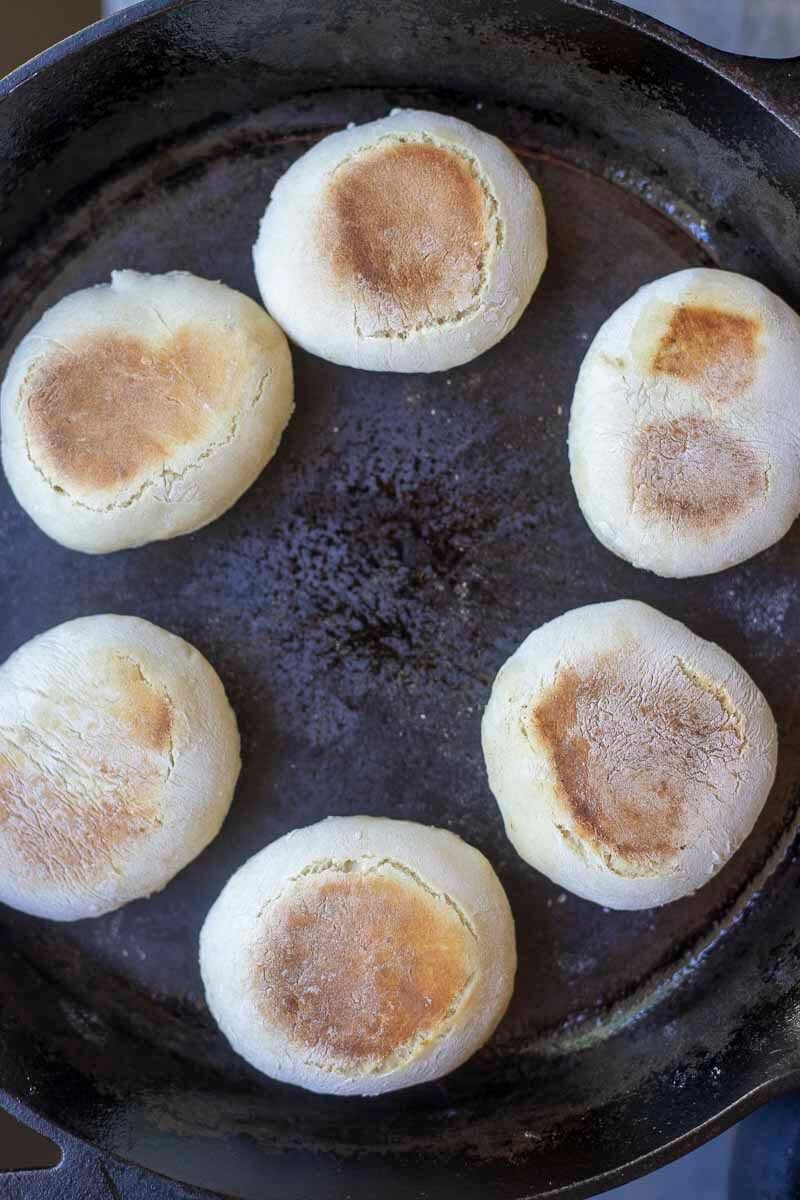 Sourdough discard English muffins cooking on a cast iron skillet.