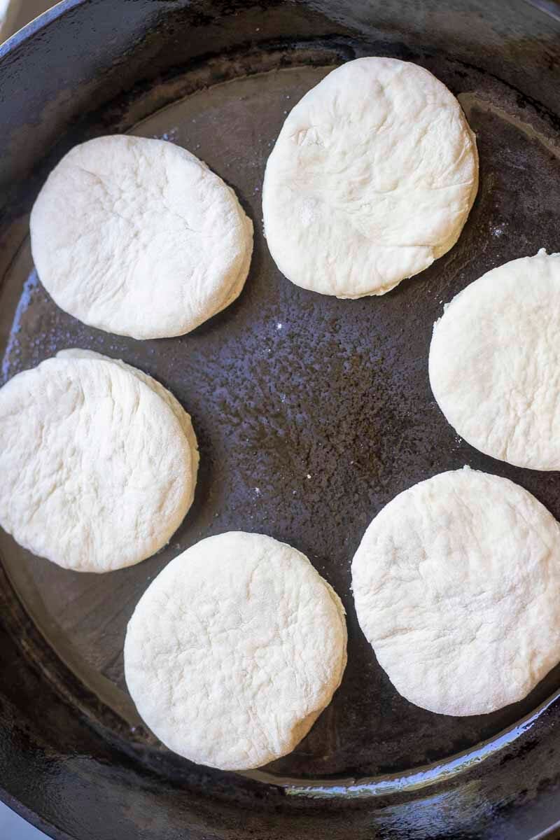 English muffin dough cooking in a cast iron skillet.