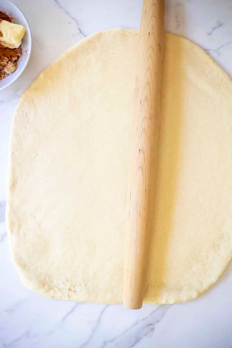 brioche dough rolled out on a countertop with a rolling pin.