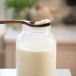 a mason jar filled with kefir with a wooden spoon resting on top with kefir grains on it.