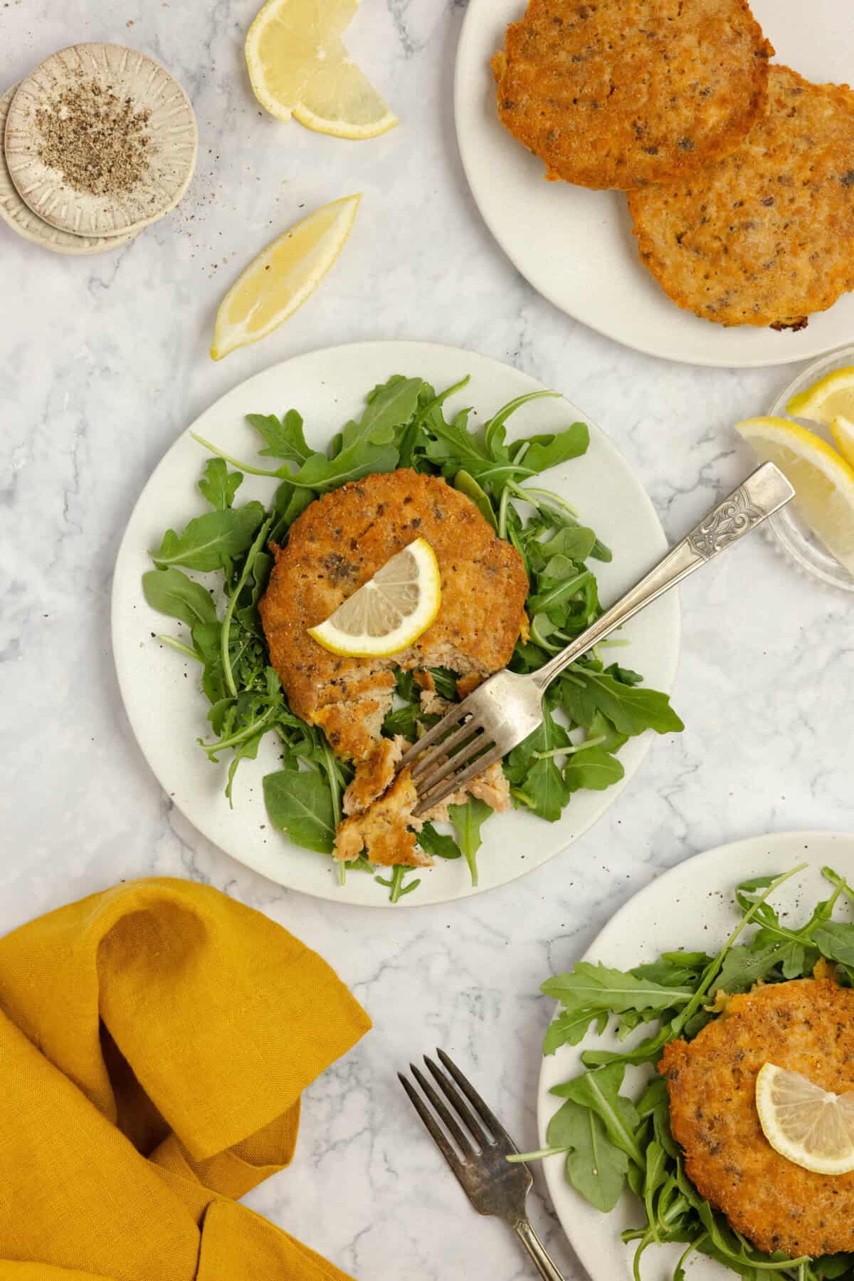 salmon croquettes on a bed of lettuce on a white plate. More salmon burgers on other plates.