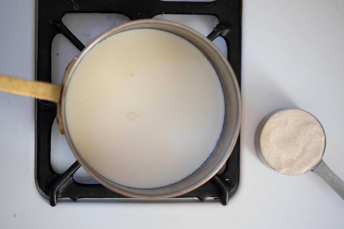 Milk in a saucepan with a measuring cup of sugar off to the side.