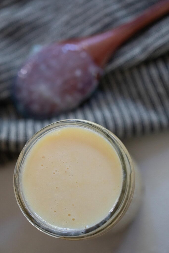 A jar full of sweetened condensed milk with a wooden spoon on the side.