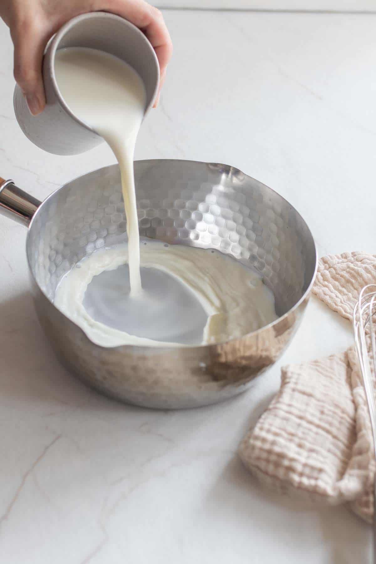 Milk being poured into a silver saucepan.