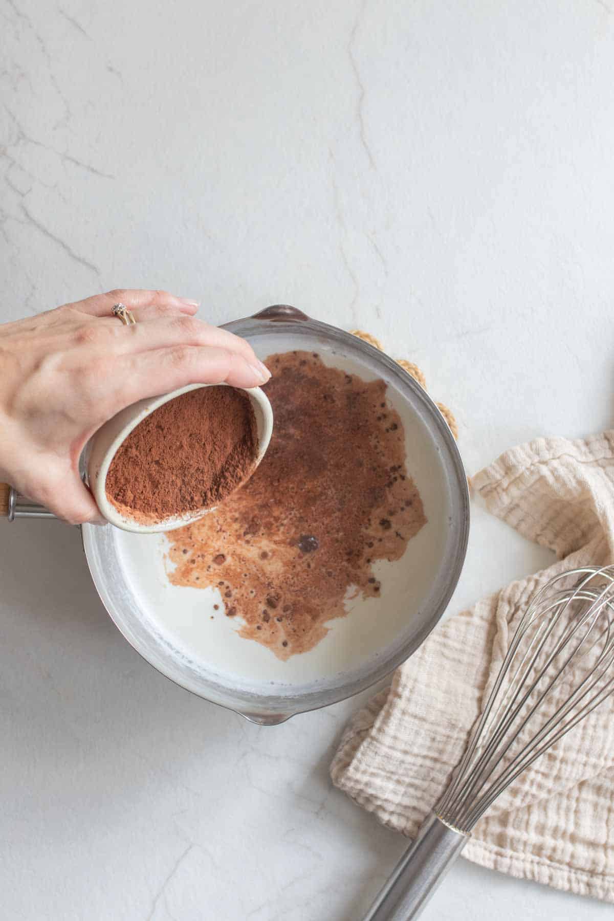 Pouring cocoa powder into a saucepan of milk.