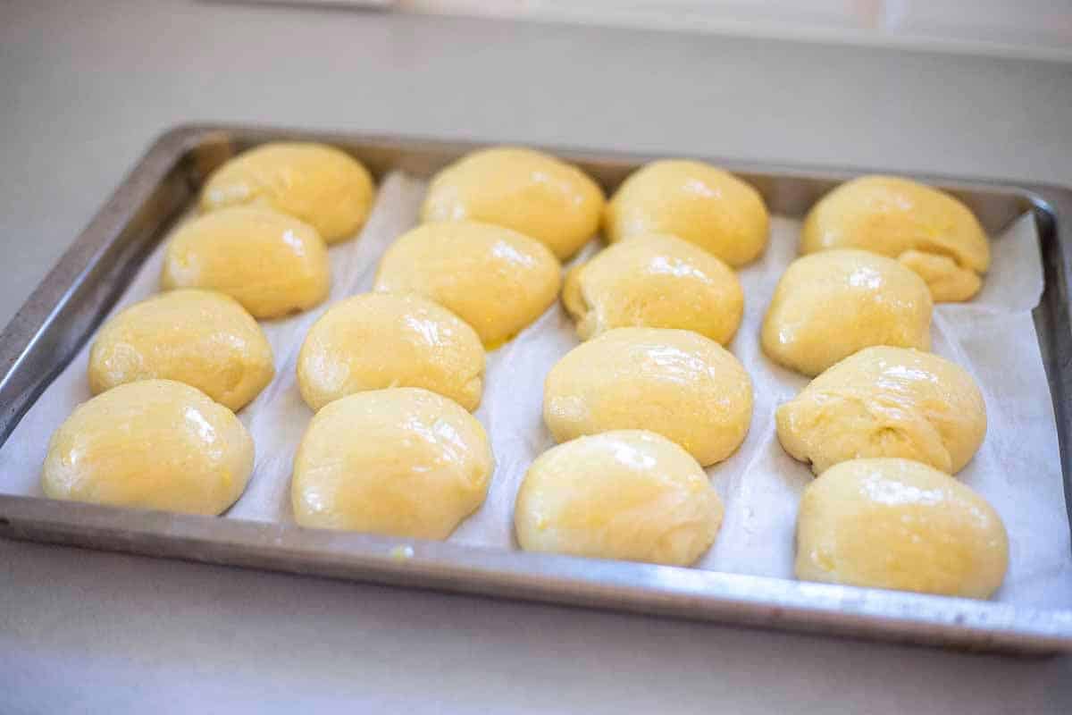 Risen rolls brushed with an egg wash on a parchment lined baking sheet.