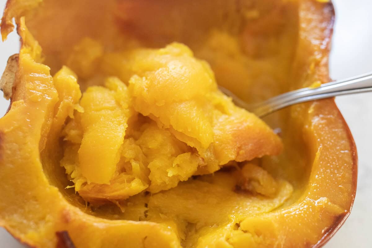 A spoon scooping out the inside of a roasted pie pumpkin.