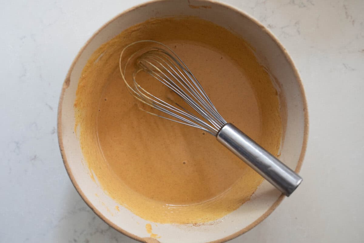Pumpkin puree and other ingredients in a bowl with a whisk.